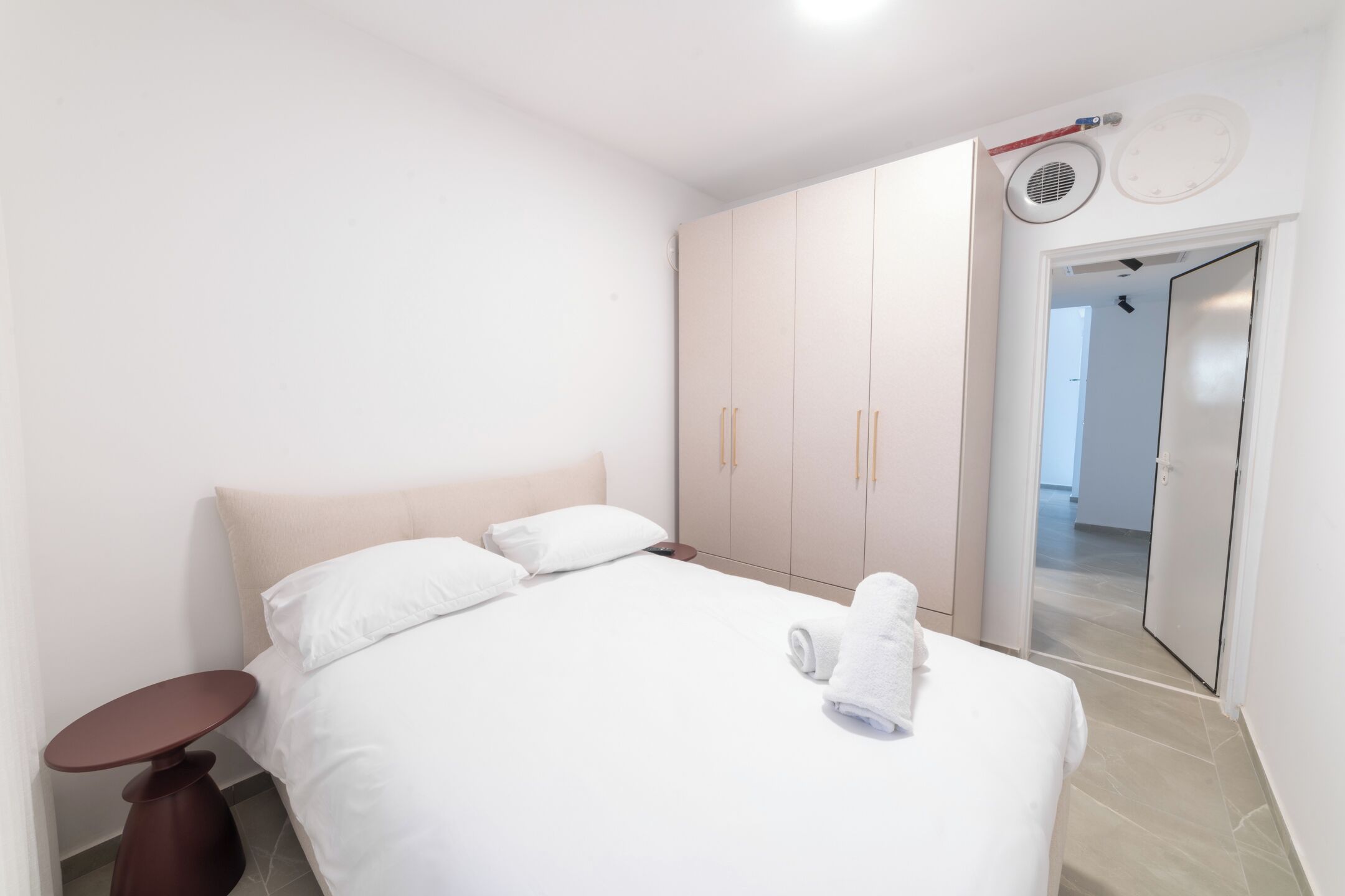 A modern hotel room with a bed, a small round table, and a wardrobe.