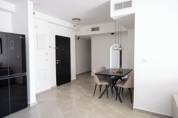 A modern kitchen with a black refrigerator, a dining table with four chairs, and a pendant light. - O&O - 2 BR Stylish & Modern Apartment (Bat Yam)