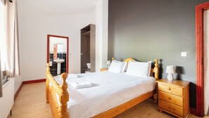 A bedroom with a wooden bed, a nightstand, a wardrobe, and a bathroom visible through an open door. - Pake's Cottage in Clahane (Liscannor)