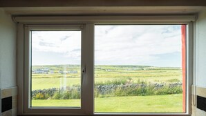 A window with a view of a green landscape and a stone wall. - Pake's Cottage in Clahane (Liscannor)