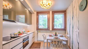 A modern kitchen with a dining table, chairs, a stove, and a window with a view of trees. - Il Mughetto Ski in / ski out (Bardonecchia)