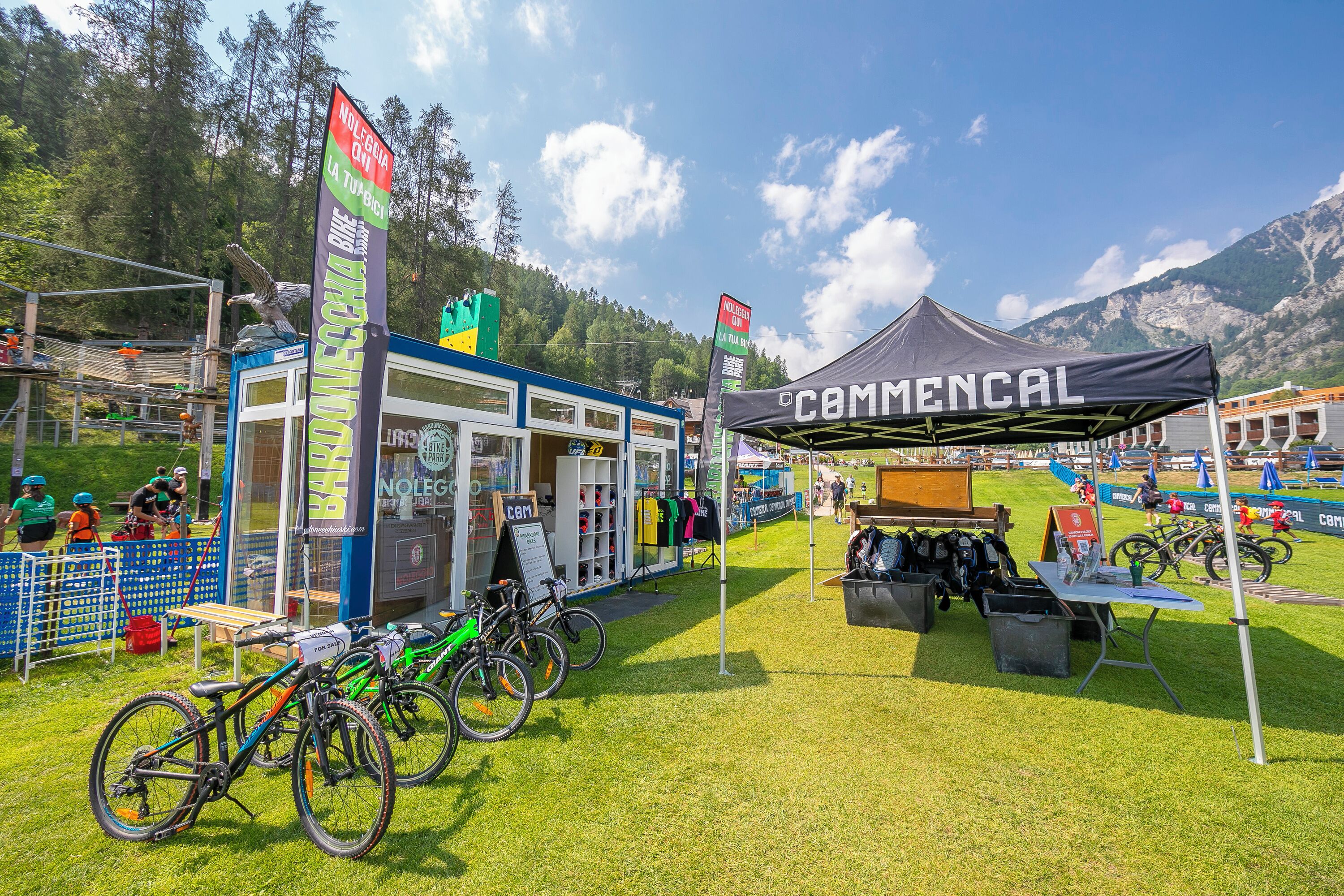 Ein Mountainbike-Event mit einem Zelt mit der Aufschrift 'Camencal', einem Geschäft namens 'NOLEGIA' und Fahrrädern, die auf der Wiese stehen.