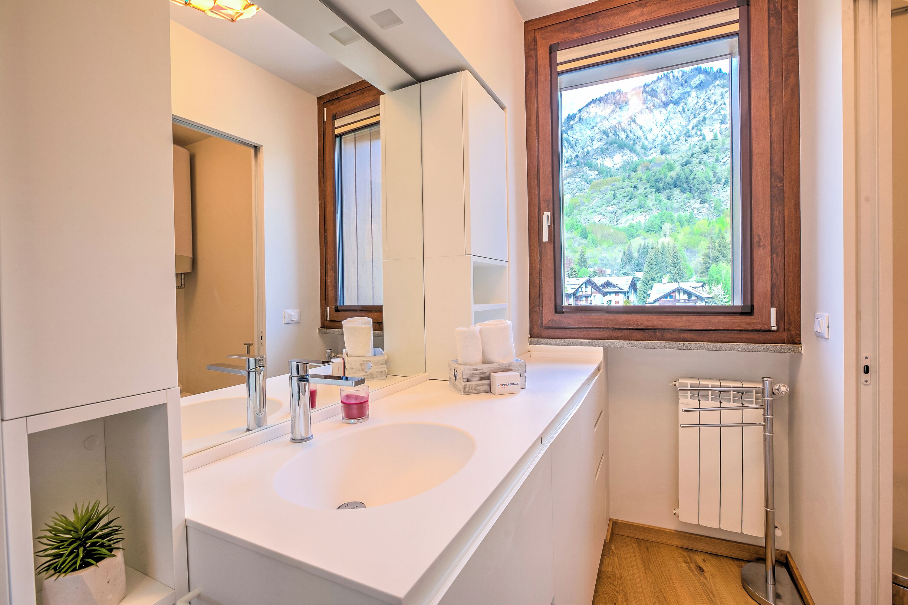 A modern bathroom with a white sink, mirror, and wooden window frame.
