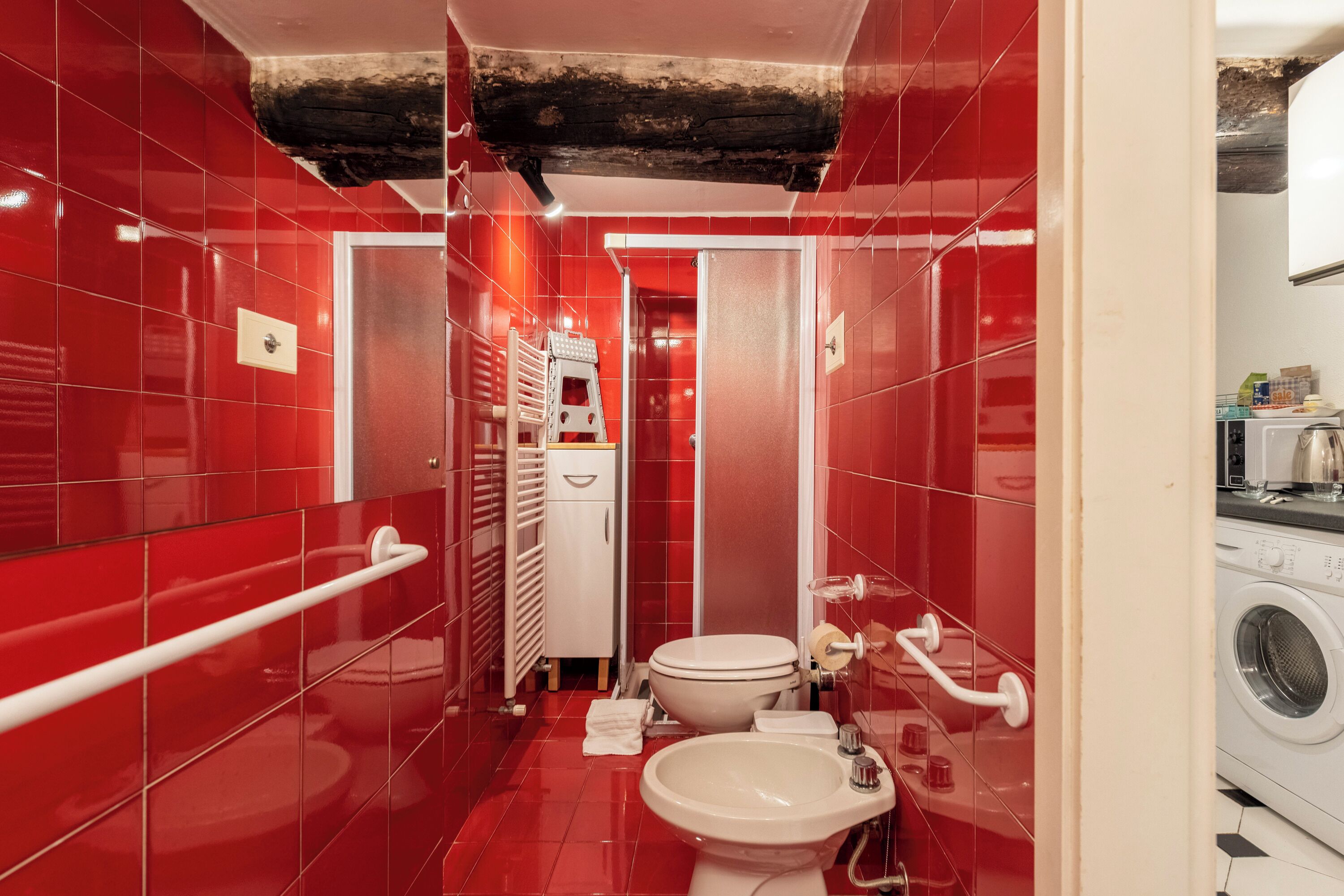 Une salle de bain avec des carreaux rouges, des toilettes blanches, un lavabo, une douche et un lave-linge.