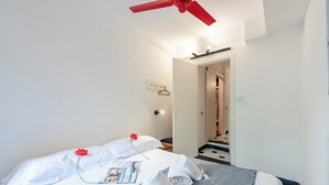 A hotel room with a bed, towels, a red ceiling fan, a light switch, and a door leading to another room. - Charming Apartment Historic Center Camogli (Camogli)