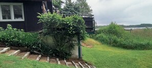Et hus med mørk facade, et synligt vindue og en have med en lille trappe til en dør.