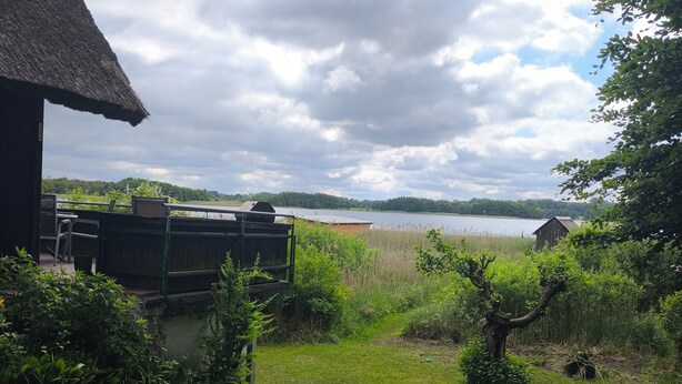 Un edificio rústico con techo de paja y vista a un lago y árboles distantes.