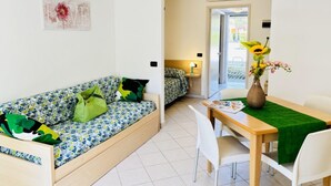 A room with a sofa, a dining table with chairs, and a small kitchen area. - Modern and Spacious Studio in Bibione (San Michele al Tagliamento)