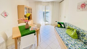 A small, bright room with a dining table, a sofa, and a cabinet. - Modern and Spacious Studio in Bibione (San Michele al Tagliamento)