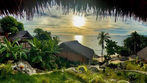 Un resort tropical con cabañas de techo de paja, exuberante vegetación y vistas al océano al atardecer.