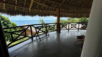 Un espacio al aire libre cubierto con vista al mar, techo de paja y barandilla de madera.