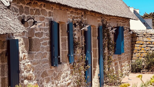 A stone building with a thatched roof and blue shutters.