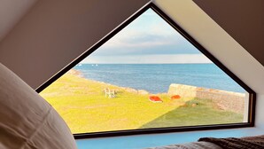 A bedroom with a large window overlooking a grassy area and the sea.