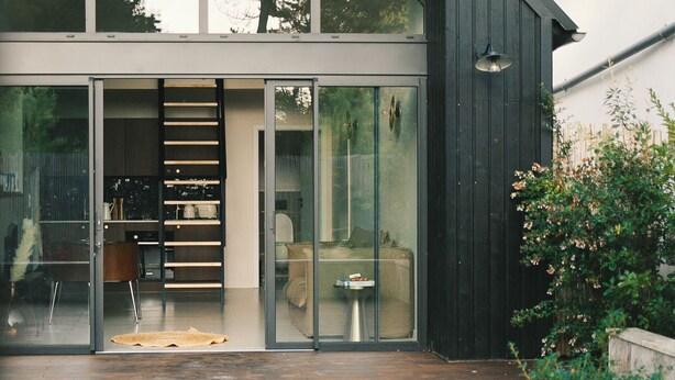 A modern house with a large glass door, a wooden deck, and a garden area.