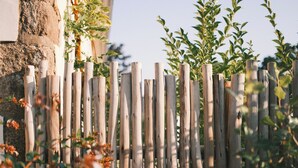 A wooden fence with vertical slats, a stone wall, and green foliage in the foreground.