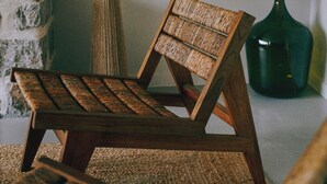 A wooden lounge chair with a woven backrest and seat, positioned on a textured rug.