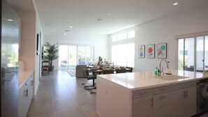 A modern kitchen with a large island, a dining area with a table and chairs, and a view of the outdoors through large windows.