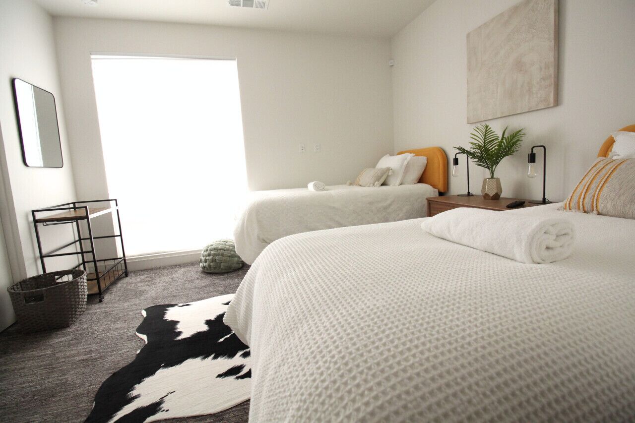 A modern hotel room with two beds, a large window, a cowhide rug, and a minimalist decor.