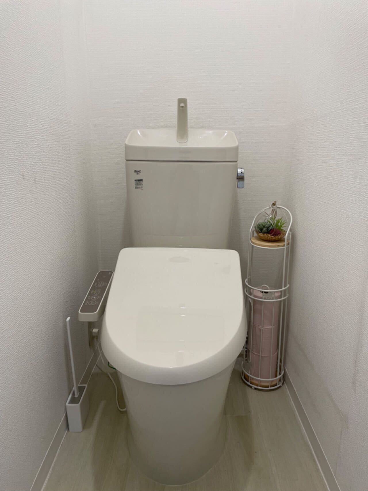A small, white toilet with a control panel and a wall-mounted trash can with a plant.