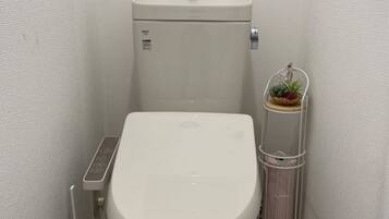 A small, white toilet with a control panel and a wall-mounted trash can with a plant.
