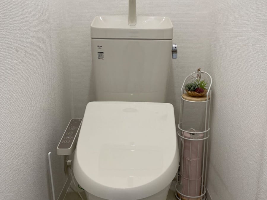 A small, white toilet with a control panel and a wall-mounted trash can with a plant.