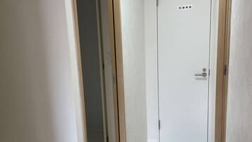 A narrow hallway with a white door at the end, wooden trim, and a light-colored floor.