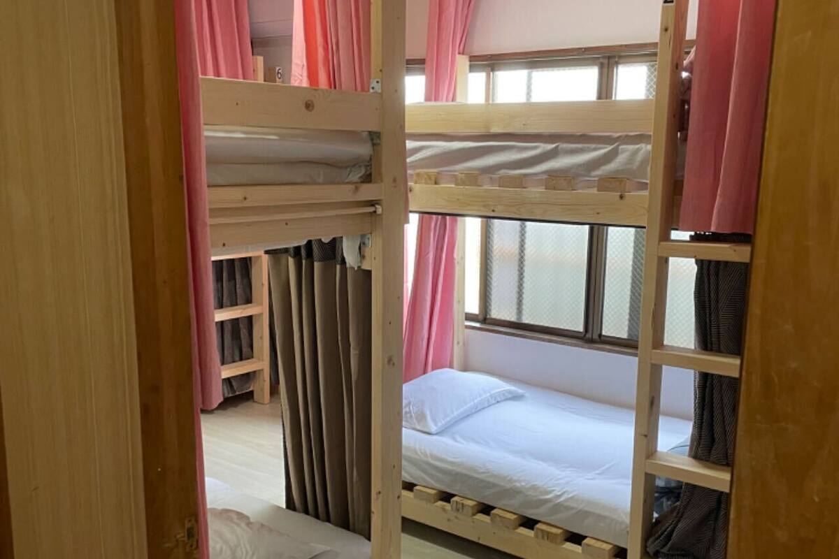 Ein Schlafzimmer mit Etagenbetten, Holzrahmen, rosa Vorhängen und einem Fenster.