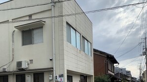 Une rue bordée d’un immeuble dont les unités de climatisation sont fixées à l’extérieur, avec un scooter garé et un passage piéton.