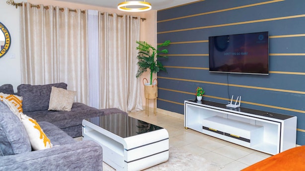 A modern living room with a grey sofa, a white coffee table, and a flat-screen TV mounted on the wall. - Lux Suites Clay City Heights Kasarani (Nairobi)