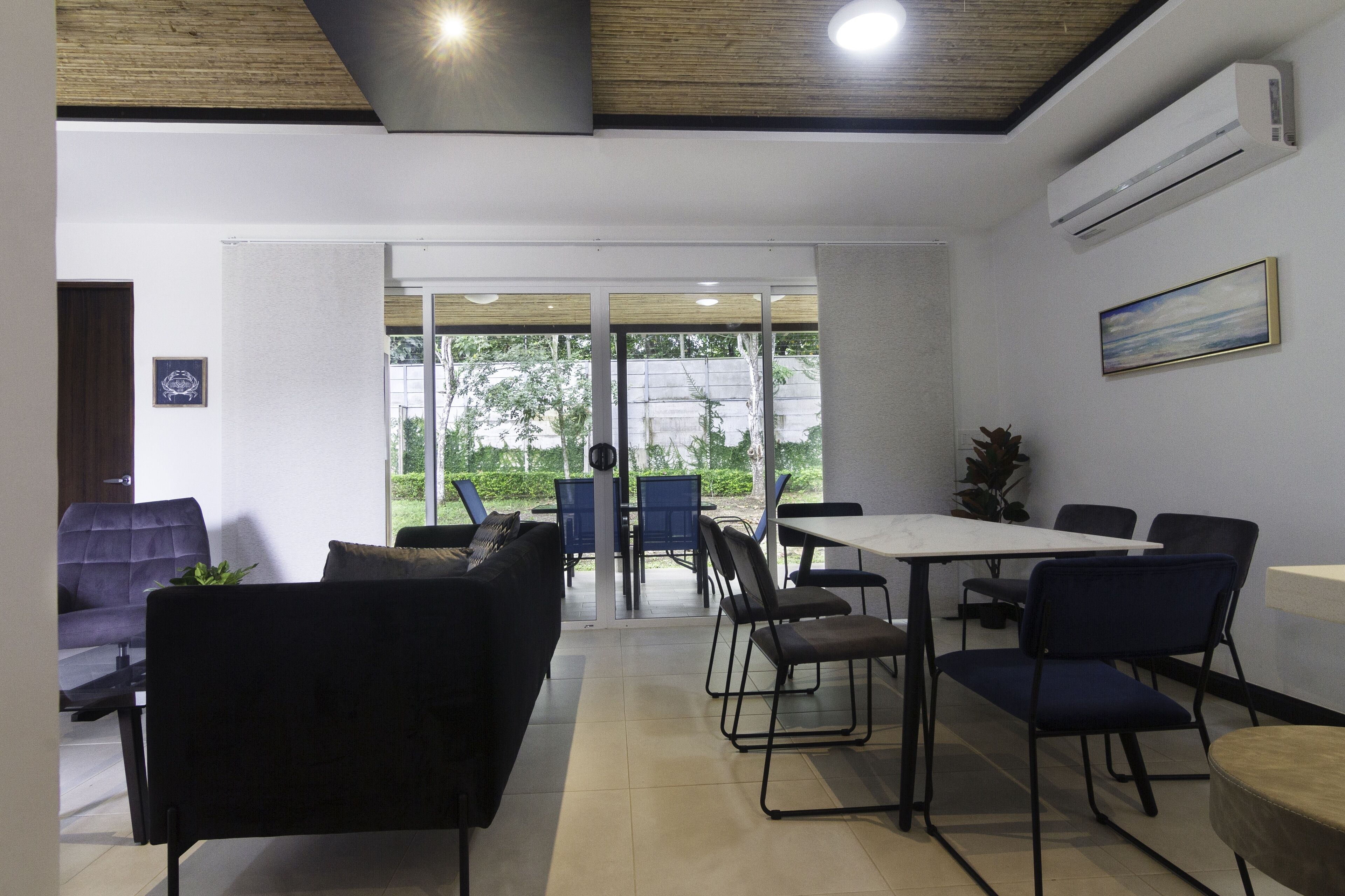 A modern indoor space with a sofa, chairs, and a table. There is a sliding glass door leading to an outdoor area.