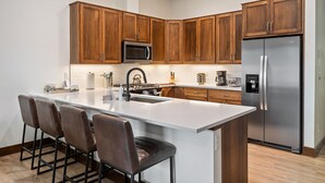 Eine moderne Küche mit Holzausstattung, einem Edelstahlkühlschrank, einer Mikrowelle und einer großen Kücheninsel mit Barhocker.