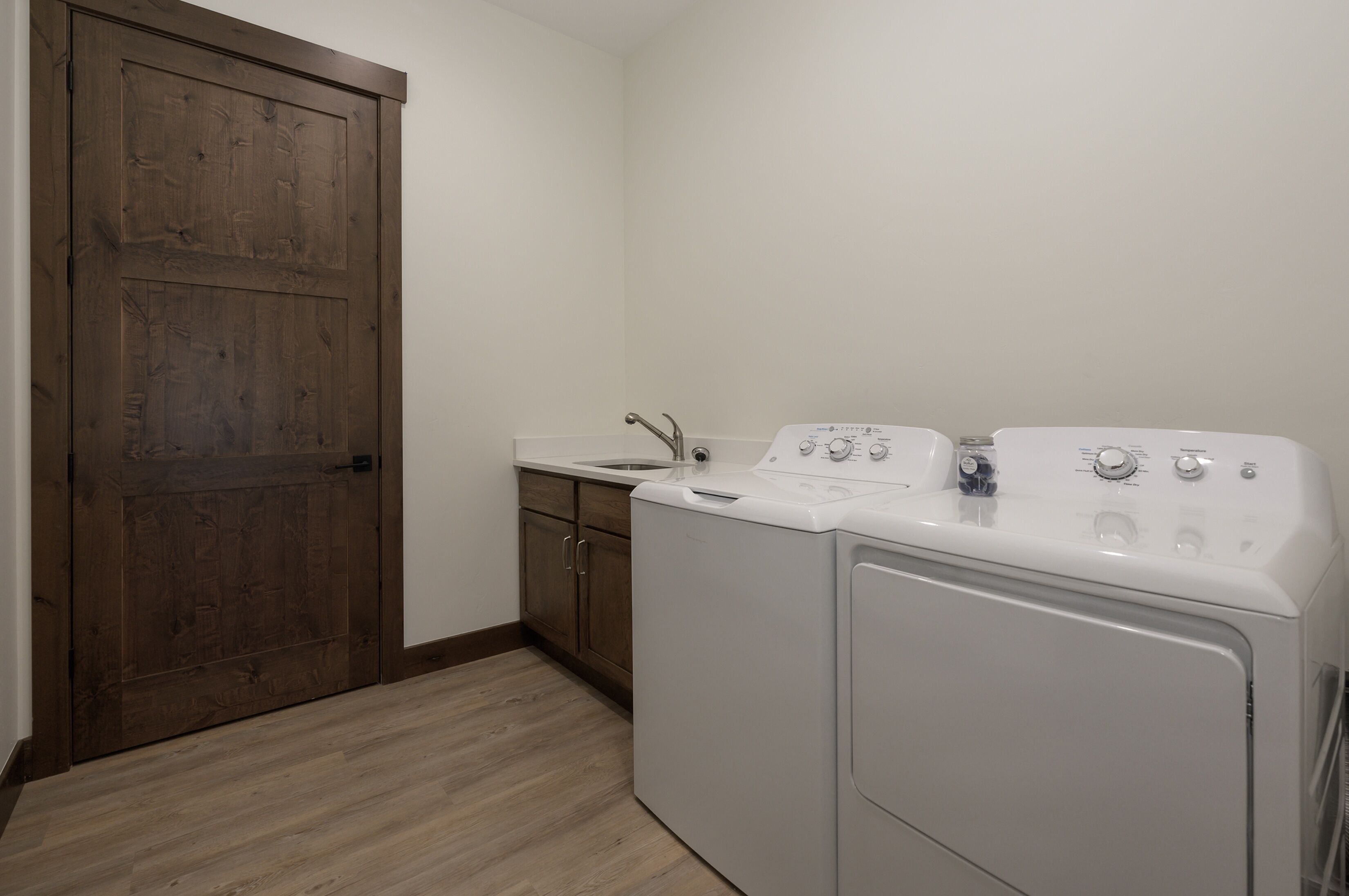 Una sala de lavandería con puerta de madera, lavadora y pileta.