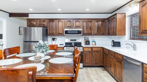 A modern kitchen with wooden cabinets, stainless steel appliances, and a dining area with a wooden table and chairs. - Becca's Place 3 Bedroom Home by RedAwning (Pigeon Forge)
