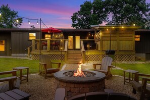 Un patio con una fogata, mobiliario exterior y una zona cubierta con guirnaldas de luces.