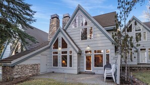 A two-story house with a stone chimney, large windows, and a stone foundation. - Summer 2026 Special - Amenities that include Pool, Steam Room, Sauna, Tennis, AC (sunriver)