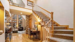 A spacious living area with a wooden staircase, stone wall, and large windows. - Summer 2026 Special - Amenities that include Pool, Steam Room, Sauna, Tennis, AC (sunriver)