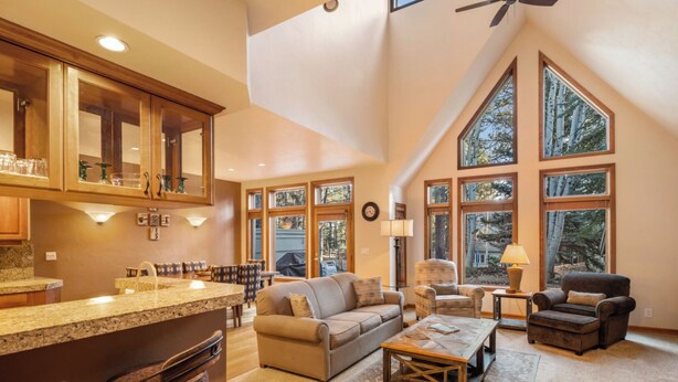 A spacious living area with a high ceiling, large windows, a kitchen with granite countertops, and a cozy seating arrangement. - Summer 2026 Special - Amenities that include Pool, Steam Room, Sauna, Tennis, AC (sunriver)