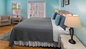 A bedroom with a bed, bedside tables, a chair, and a window with blinds. - THALIA'S RETREAT @ Duval Square 2bd/2ba townhome (Key West)