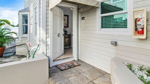 A residential entryway with a door leading to an interior, a fire extinguisher mounted on the wall, and a potted plant outside. - THALIA'S RETREAT @ Duval Square 2bd/2ba townhome (Key West)