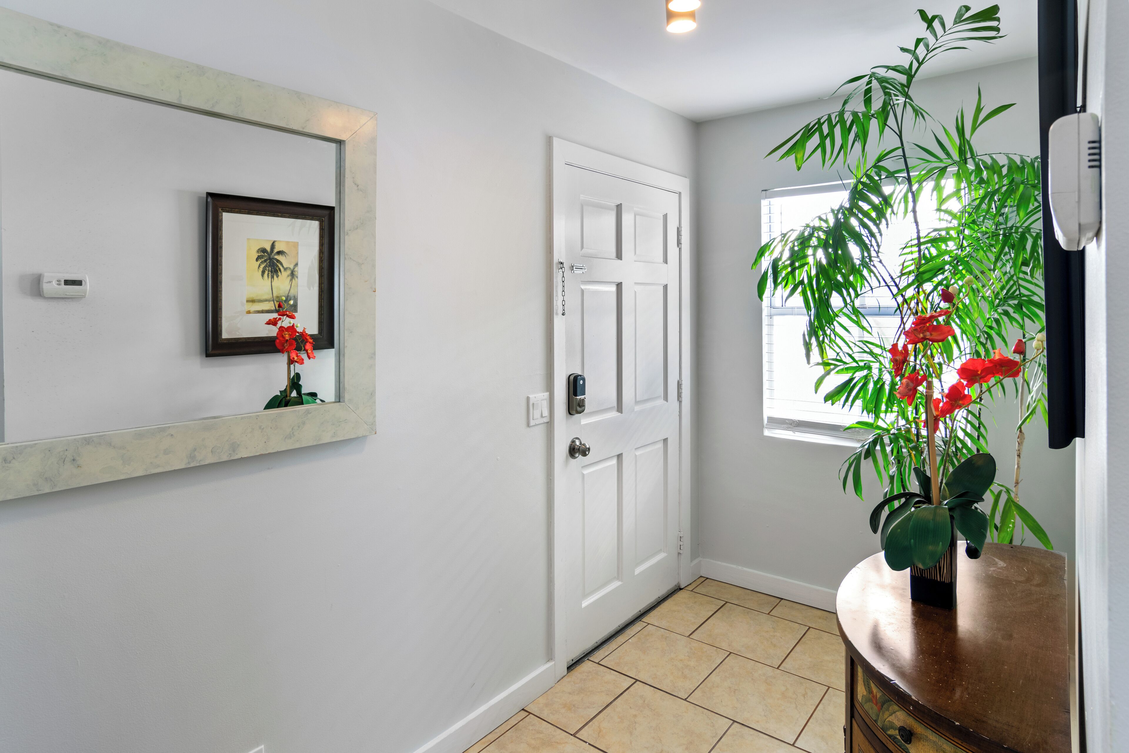 Un couloir avec une porte blanche, un tableau encadré accroché au mur et une plante en pot ornée de fleurs rouges.