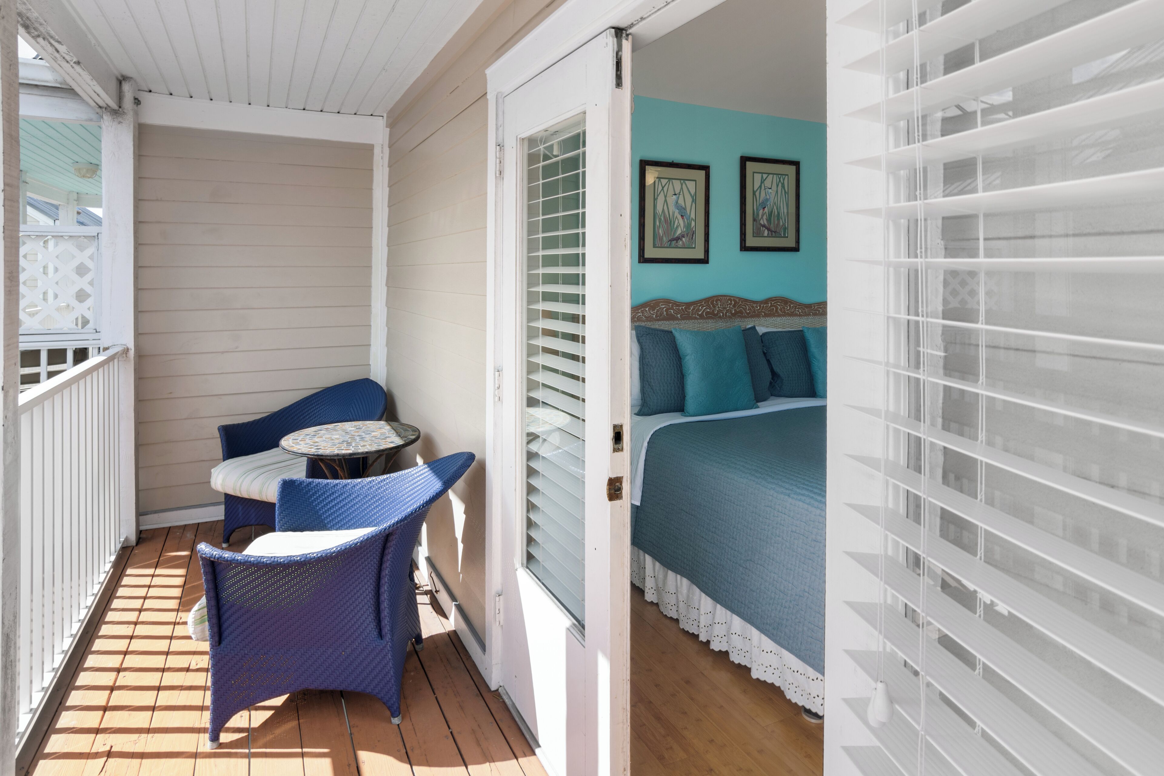Een balkon met rieten meubels, een bed met blauw beddengoed en een raam met zonwering.