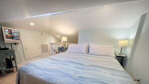 A bedroom with a bed, two bedside tables with lamps, a desk with a computer, and a TV on the wall. - Rent at PORCHSIDE PARADISE - Steps to Duval (Key West)