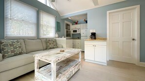 Un espace de vie compact comprenant un canapé, une table basse, un coin cuisine avec des placards et une porte.