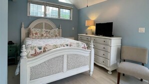 Une chambre à coucher comprenant un lit, une commode, une chaise, un ventilateur de plafond et des fenêtres.