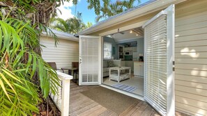 Un patio exterior acogedor con cubierta de madera, una mesa blanca y una zona de estar con cojines.