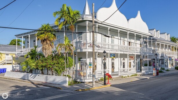 A white colonial-style building with balconies, palm trees, and a street view. - LA CASA CUBANA @ Cuban Club Suites (Key West)