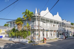 Un edificio de estilo colonial blanco con balcones, palmeras y vista a la calle.