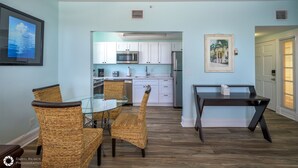A modern kitchen with white cabinets, stainless steel appliances, and a dining area with wicker chairs and a glass table. - LA CASA CUBANA @ Cuban Club Suites (Key West)