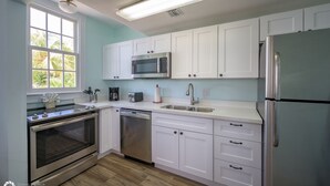 A modern kitchen with white cabinets, stainless steel appliances, and a window with a view of greenery. - LA CASA CUBANA @ Cuban Club Suites (Key West)