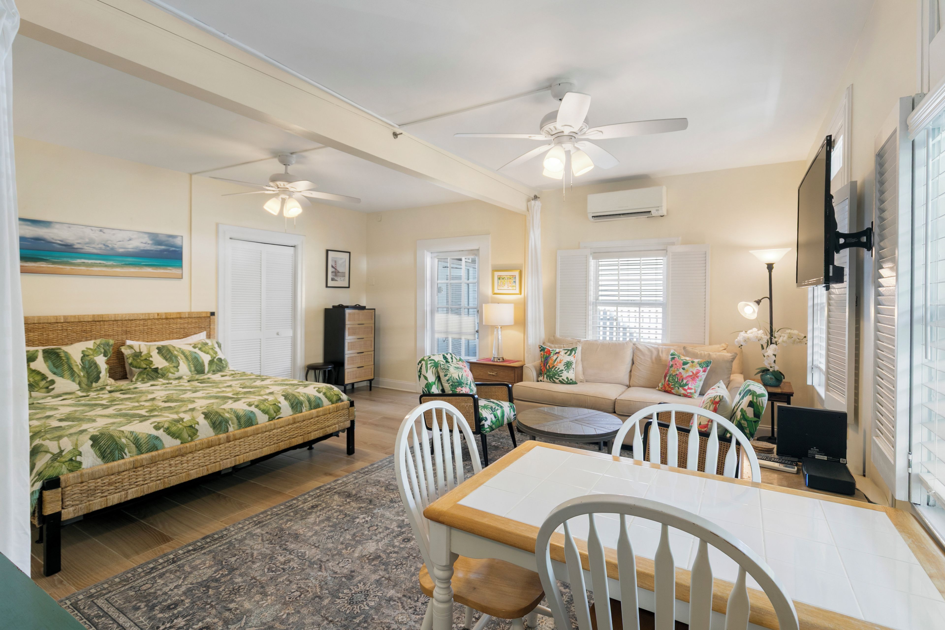 A well-lit room with a bed, a dining table, chairs, a sofa, and a ceiling fan.